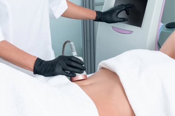 Practitioner in black gloves performs abdominal body contouring using a handheld device in a clinic setting.