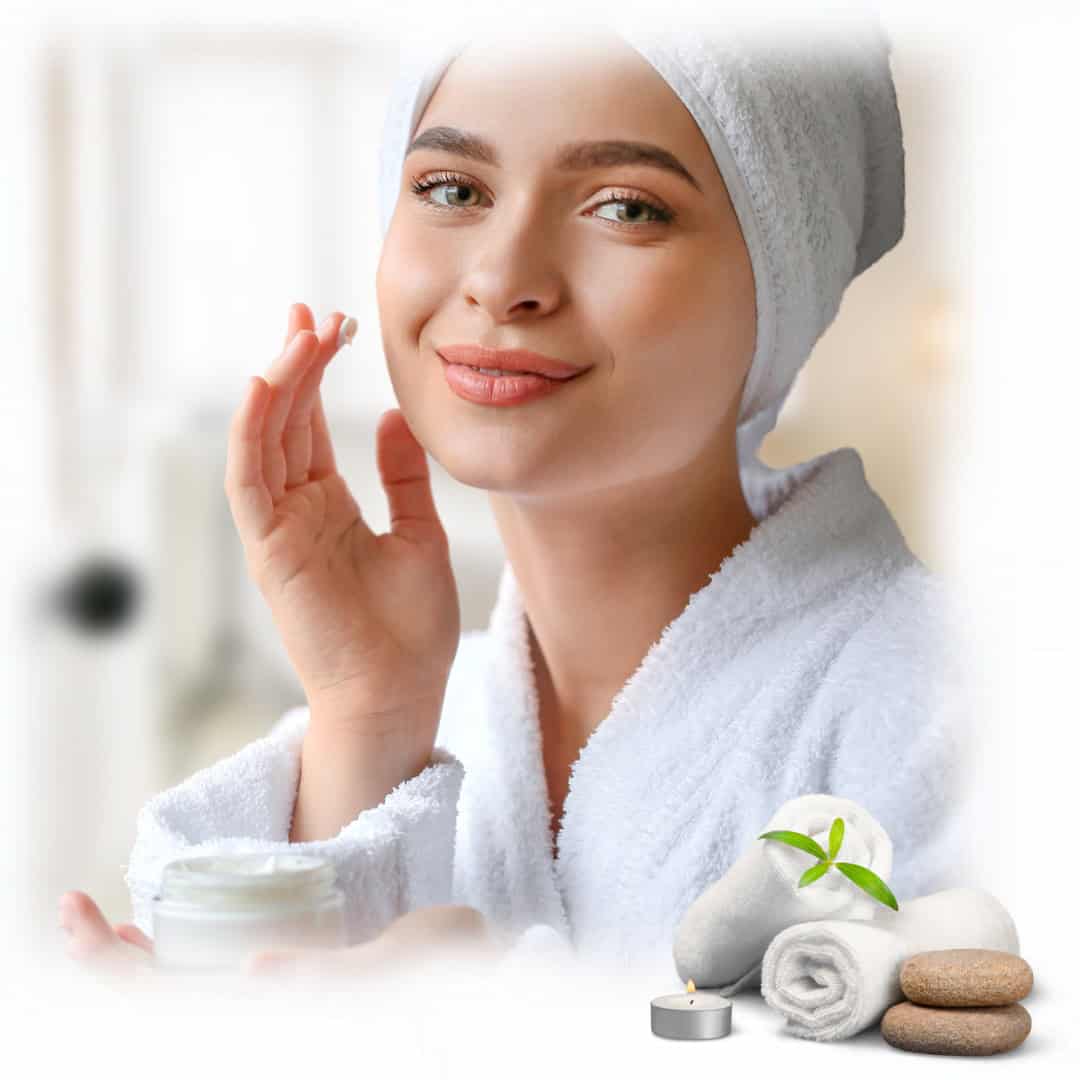 Woman in bathrobe applies face cream, spa items and candle nearby, showcasing a relaxing Anchorage spa experience.