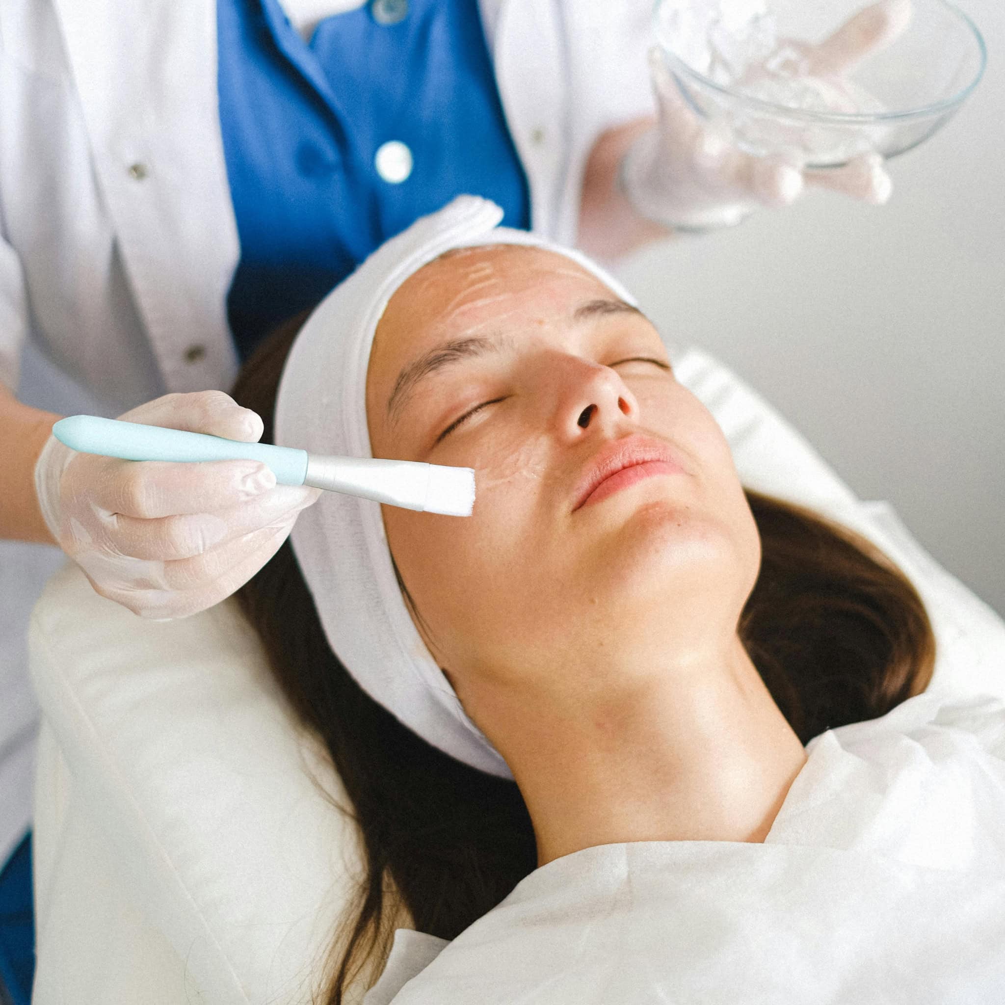 A person with eyes closed gets a facial mask applied at a medical spa in Anchorage by a gloved professional using a brush.