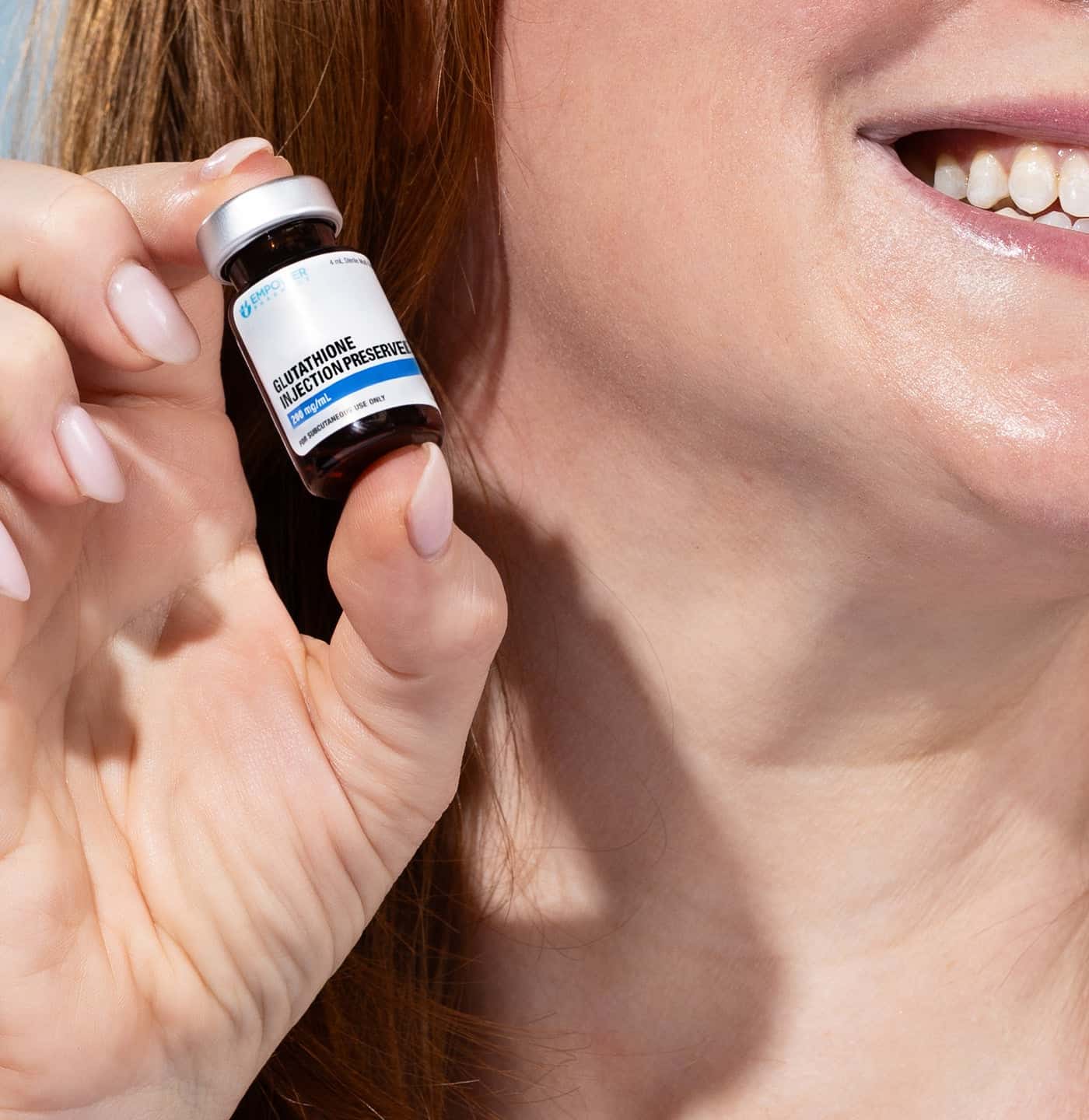 Person smiling and holding a small “Glutathione Injection/Preservative” bottle near their face.