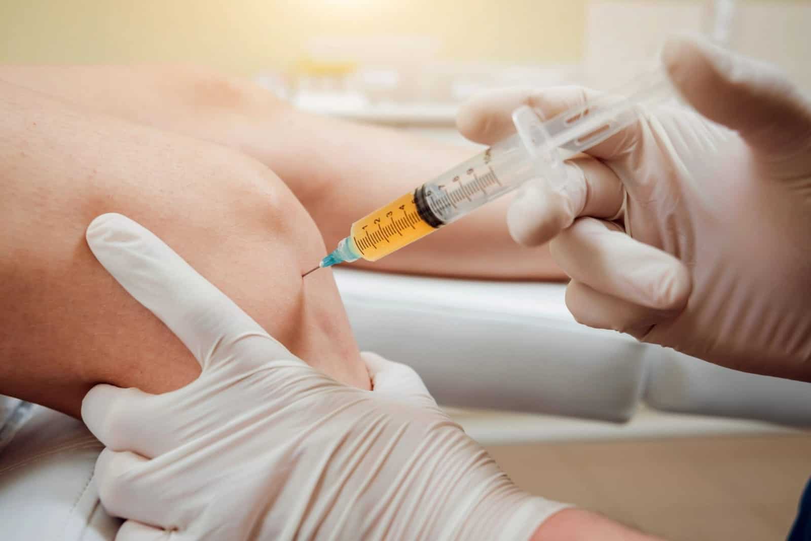 Doctor in gloves gives an injection into a patient’s knee, likely for treatment or pain relief.